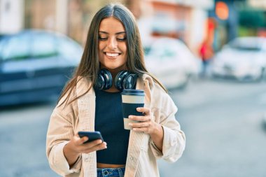 Genç İspanyol kız akıllı telefon kullanıyor ve parktaki kahveleri içiyor. Şehirde..