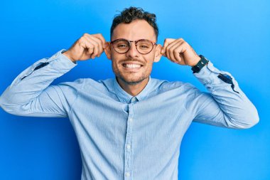 Günlük kıyafetler ve gözlük takan genç İspanyol adam gülümsüyor kulakları parmaklarıyla çekiyor, komik bir jest. deneme sorunu 