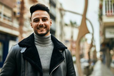 Genç Arap adam gülümsüyor, mutlu bir şekilde şehirde duruyor..