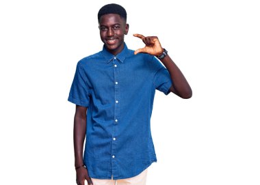 Gündelik kıyafetler giyen, gülümseyen, kendine güvenen, el hareketi yapan, parmaklarıyla işaret yapan ve kameraya bakan genç Afro-Amerikan bir adam. ölçüm kavramı. 