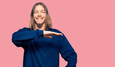 Uzun saçlı, sıradan bir kazak giyen, elleri büyük ve büyük bir işaret gösteren yakışıklı, beyaz bir adam. Kameraya bakıp gülümsüyor. ölçüm kavramı. 