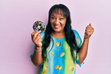 Orta yaşlı Afro-Amerikalı kadın elinde donutla gururla bağırıyor zaferi ve başarıyı kutluyor. 