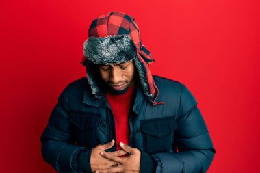 Sakallı, kışlık şapkalı ve eli midesinde olan Afrikalı genç bir Amerikalı adam. Çünkü hazımsızlık, acı verici bir hastalık ve kendini iyi hissetmiyor. Ağrı kavramı. 