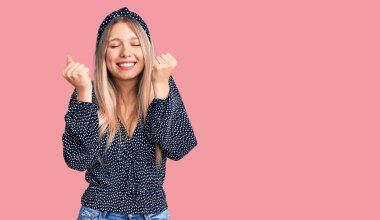 Başarı için heyecanlı, kolları havada ve gözleri kapalı, gündelik giysiler giyen genç, güzel sarışın kadın zaferi kutluyor. Kazanan konsept. 