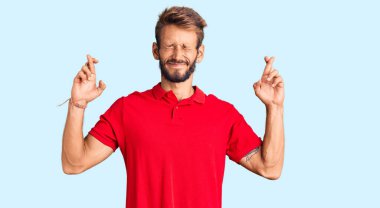 Sarışın, sakallı, sıradan kıyafetler giyen, umut dolu ve gözleri kapalı bir şekilde el işareti yapan yakışıklı bir adam. Şans ve batıl inançlar. 