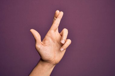 İzole edilmiş mor arka plan üzerinde parmaklarını gösteren beyaz bir gencin eli. Parmakları çapraz, batıl inançlar ve şanslı bir jest, şanslı ve umut dolu bir ifade.