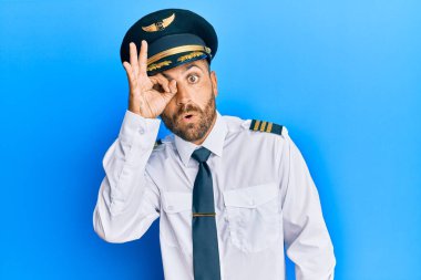 Uçak pilotu üniforması giyen sakallı yakışıklı adam şaşırmış yüz ifadesiyle şaşırmış, parmaklarından bakan gözler. İnançsız ifade. 
