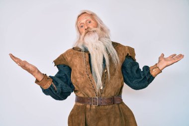 Gri saçlı, uzun sakallı, Viking kostümü giyen, kafası karışmış ve kolları ve elleri havada yaşlı bir adam. şüphe kavramı. 