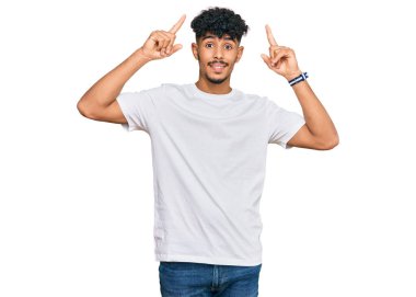 Gündelik beyaz tişört giyen genç Arap adam şaşkın şaşkın ve şaşırmış bir şekilde parmaklarıyla işaret ediyor ve kollarını kaldırıyordu.. 