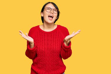 Kısa saçlı, kısa saçlı, gözlüklü, çılgın ve çılgın başarısını kutlayan genç, İspanyol bir kadın. Kolları havada, gözleri kapalı, heyecanlı bir şekilde bağırıyor. Kazanan konsept 