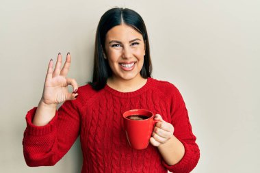 Güzel esmer kadın bir fincan sade kahve içiyor parmaklarıyla imza atıyor, gülümseyerek mükemmel bir sembol oluşturuyor. 