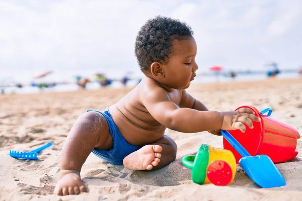 愛らしいアフリカ系アメリカ人の幼児はおもちゃで遊んでいます砂の上に座ってビーチ — ストック写真