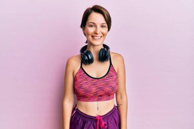 Kısa saçlı, spor giyimli, kulaklık takan mutlu ve havalı bir gülümsemesi olan esmer bir kadın. şanslı kişi. 