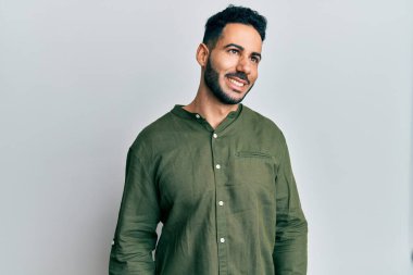 Gündelik kıyafetler giyen genç İspanyol bir adam yüzünde gülümsemeyle yan yana bakıyor, doğal bir ifade. Kendinden emin gülen. 