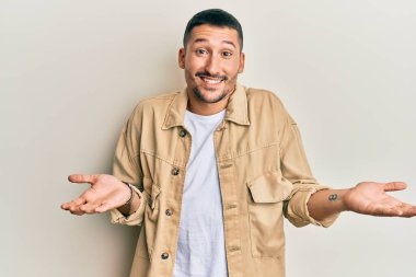 Sıradan kahverengi kot ceket giyen, elleri ve kolları havada, kafası karışmış ve kafası karışık, yakışıklı bir adam. şüphe kavramı. 