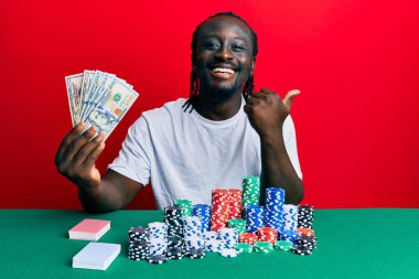 Elinde 100 dolarlık banknotlarla poker oynayan yakışıklı siyahi bir adam başparmağını kaldırıyor ve ağzı açık gülümsüyor. 