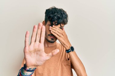 Latin kökenli genç bir adam, günlük kıyafetler giyip, elleriyle gözlerini kapatıyor ve üzgün ve korku ifadeleriyle jestleri durduruyor. utangaç ve olumsuz kavram. 