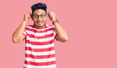 Yakışıklı Latin Amerikalı genç adam günlük kıyafetler ve gözlük takıyor gülümsüyor kulakları parmaklarıyla çekiyor, komik bir jest. deneme sorunu 