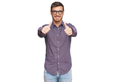 Yakışıklı, günlük kıyafetler giyen ve gözlük takan beyaz bir adam. Elle olumlu jest yapıyor, gülümsüyor ve başarı için seviniyor. kazanan jest. 