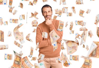 Sıradan kıyafetler giyen, kameraya kendinden emin, kolları çapraz ve çenesi havada gülümseyen genç yakışıklı bir adam. Olumlu düşünmek.