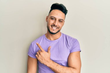 Genç Arap adam gündelik giysiler giyiyor. Gülümsüyor, elleri ve parmakları yana doğru uzanıyor. 