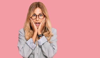 İş kıyafetleri giymiş güzel sarışın bir kadın. Korkmuş ve şok olmuş. Şaşırmış ve şaşırmış bir ifade. 