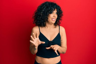 Kolsuz tişörtlü, sıradan giyinen genç İspanyol kadın tiksindirici ve tiksindirici bir ifade takınıyor çünkü tiksinti tepki veriyor. Eller havada. 