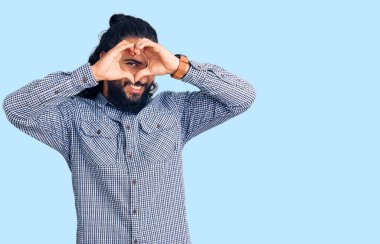 Gündelik giysiler giyen genç bir Arap. El ve parmaklarıyla kalp şeklinde. Tabelanın içinden bakıp gülümsüyor. 