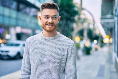 Genç beyaz adam gülümseyerek şehirde mutlu mesut duruyor..