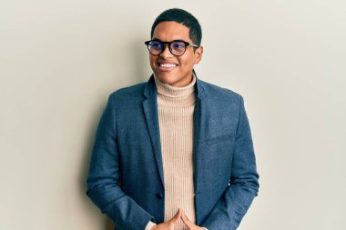 Zarif kıyafetler ve gözlük takan yakışıklı İspanyol bir adam yüzünde gülümseme, doğal bir ifade ile yan yana bakıyor. Kendinden emin gülen. 