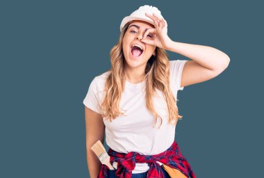 Güvenlik kaskı takan, el hareketleriyle gülümseyen, mutlu yüzüyle parmaklarının arasından bakan beyaz bir kadın.. 