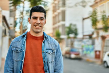 Genç İspanyol adam gülümseyerek şehirde mutlu mesut dikiliyor..