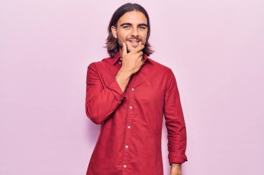 İş kıyafetleri giymiş genç bir adam kameraya kendinden emin bakıyor kollarını kavuşturmuş ve çenesini kaldırmış gülümsüyor. Olumlu düşünmek. 