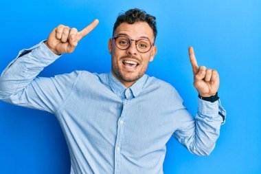 Gündelik kıyafetler ve gözlük takan genç İspanyol adam şaşkın şaşkın ve şaşırmış bir şekilde parmaklarıyla işaret ediyor ve kollarını kaldırıyordu.. 