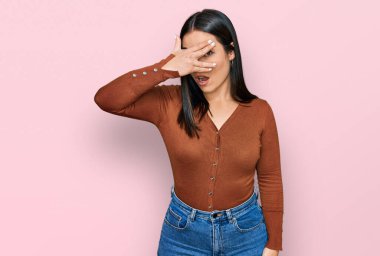 Gündelik kıyafetler giyen genç İspanyol kadın şok içinde yüzünü ve gözlerini kapayarak utanmış ifadesiyle parmaklarının arasından bakıyor.. 