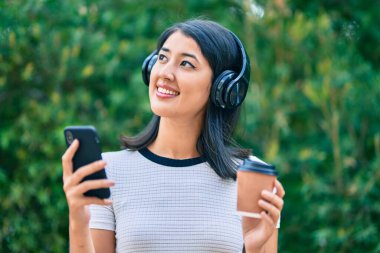 Genç İspanyol kadın kahve içiyor ve şehirde akıllı telefon ve kulaklık kullanıyor..