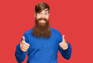 Genç İrlandalı kızıl adam, günlük kıyafetler giyiyor başarı işareti yapıyor, elleriyle olumlu jest yapıyor, gülümsüyor ve mutlu. Neşeli ifade ve kazanan jest. 