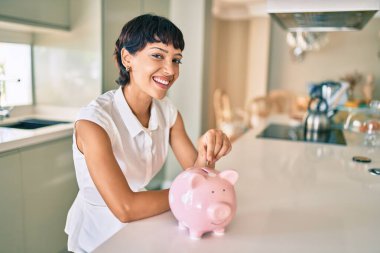 Genç esmer kadın gülümsüyor mutlu bir şekilde kumbaranın içine para koyuyor