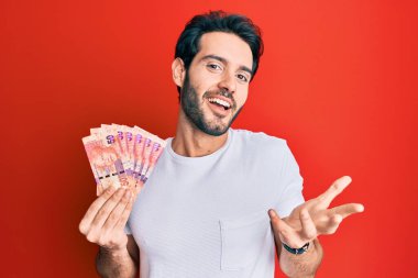 Güney Afrika Rand 'i elinde tutan İspanyol asıllı genç adam başarıyı mutlu bir gülümsemeyle ve elini kaldırarak kutluyor. 