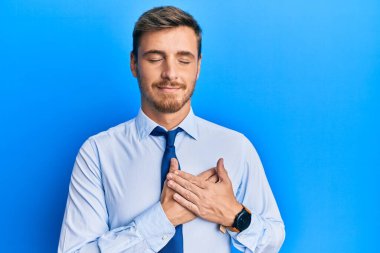 İş gömleği ve kravat takan yakışıklı beyaz adam elleri göğsünde, gözleri kapalı gülümseyen ve yüzünde minnet ifadesi olan. sağlık kavramı. 