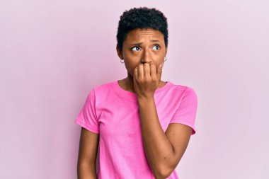 Rahat kıyafetler giyen genç Afro-Amerikalı kız elleri ağızda tırnak yerken stresli ve gergin görünüyor. anksiyete. 