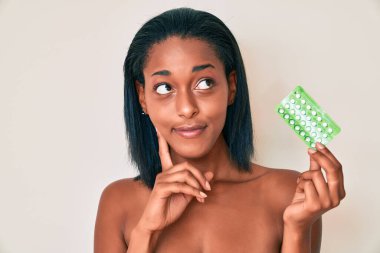 Genç Afro-Amerikalı kadın elinde doğum kontrol haplarıyla ciddi bir yüz ifadesi var. Çene ve çene üzerine soru sormayı düşünüyor. Kafa karıştırıcı bir fikir. 