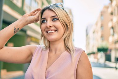 Genç sarışın kadın gülümseyerek şehirde mutlu mesut yürüyor..