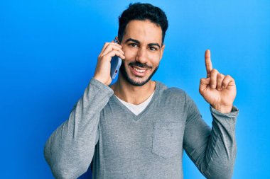 Genç İspanyol bir adam akıllı telefondan konuşuyor. Bir fikir veya soruyla gülümsüyor. Mutlu bir yüzle işaret ediyor. 