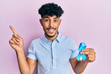 Genç Arap yakışıklı adam mavi kurdele tutuyor gülümsüyor mutlu eli ve parmağı yana bakıyor 