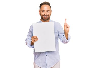 Boş afiş tutan yakışıklı orta yaşlı bir adam bir fikre ya da soru işaretine şaşırmış ve mutlu bir yüzle işaret ediyor. 