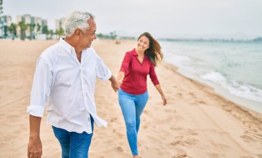 Orta yaşlı İspanyol çift kumsalda yürürken mutlu bir şekilde gülümsüyor..