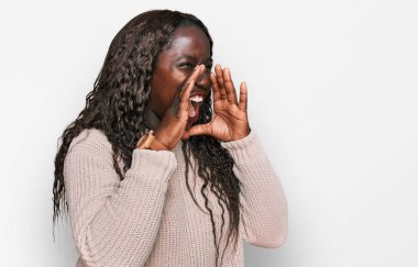 Yün kazak giyen genç Afrikalı kadın elleri ağızda bağırarak bağırıyor. 