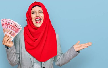 Güzel İspanyol kadın İslami tesettüre bürünmüş elinde Çin Yuan banknotları ile zaferi kutluyor mutlu bir gülümsemeyle ve ellerini kaldırarak kazanan bir ifadeyle. 
