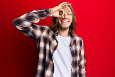 Handsome caucasian man with long hair wearing casual clothes smiling happy doing ok sign with hand on eye looking through fingers 